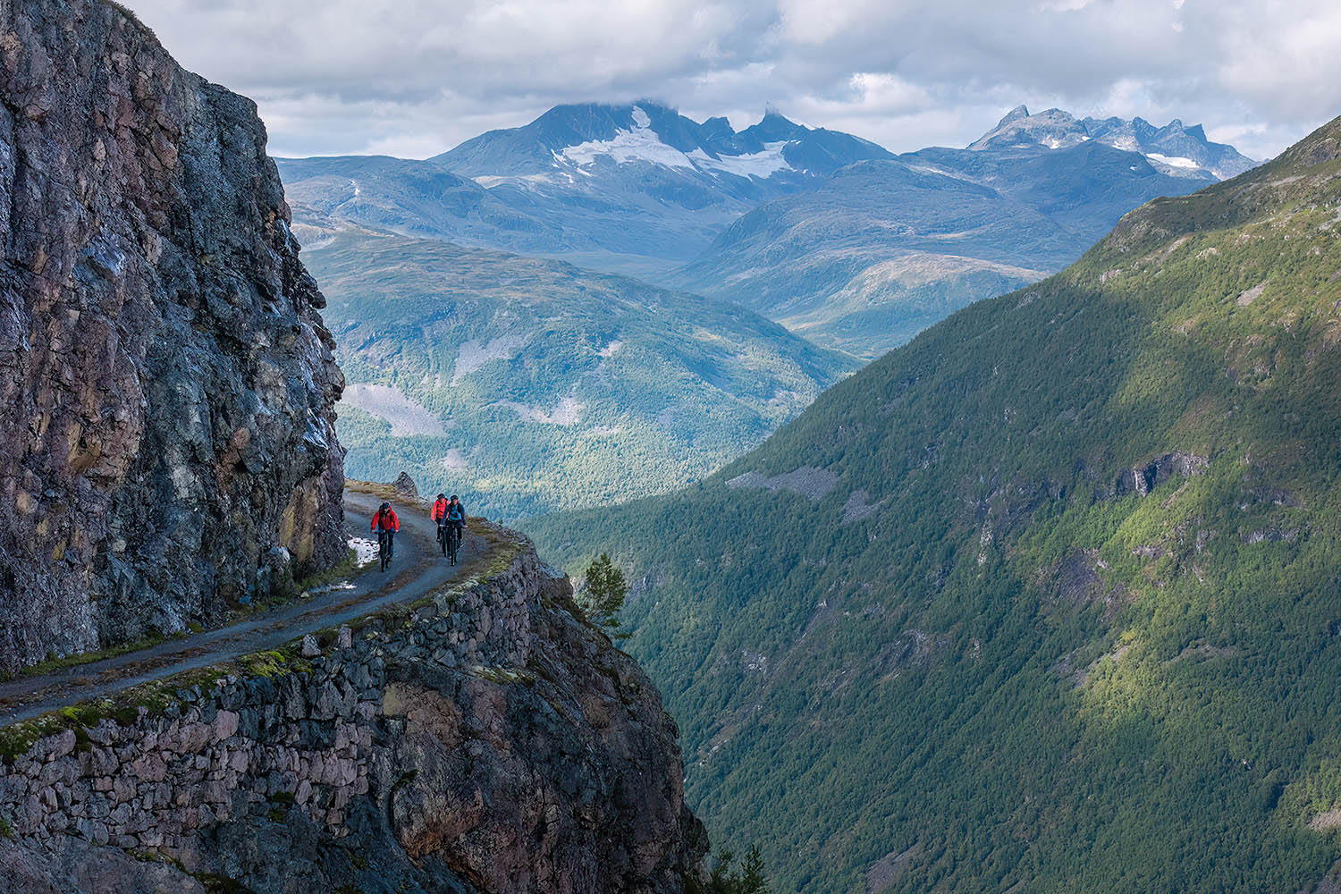 Cyclists on an old road with abyss and high mountains