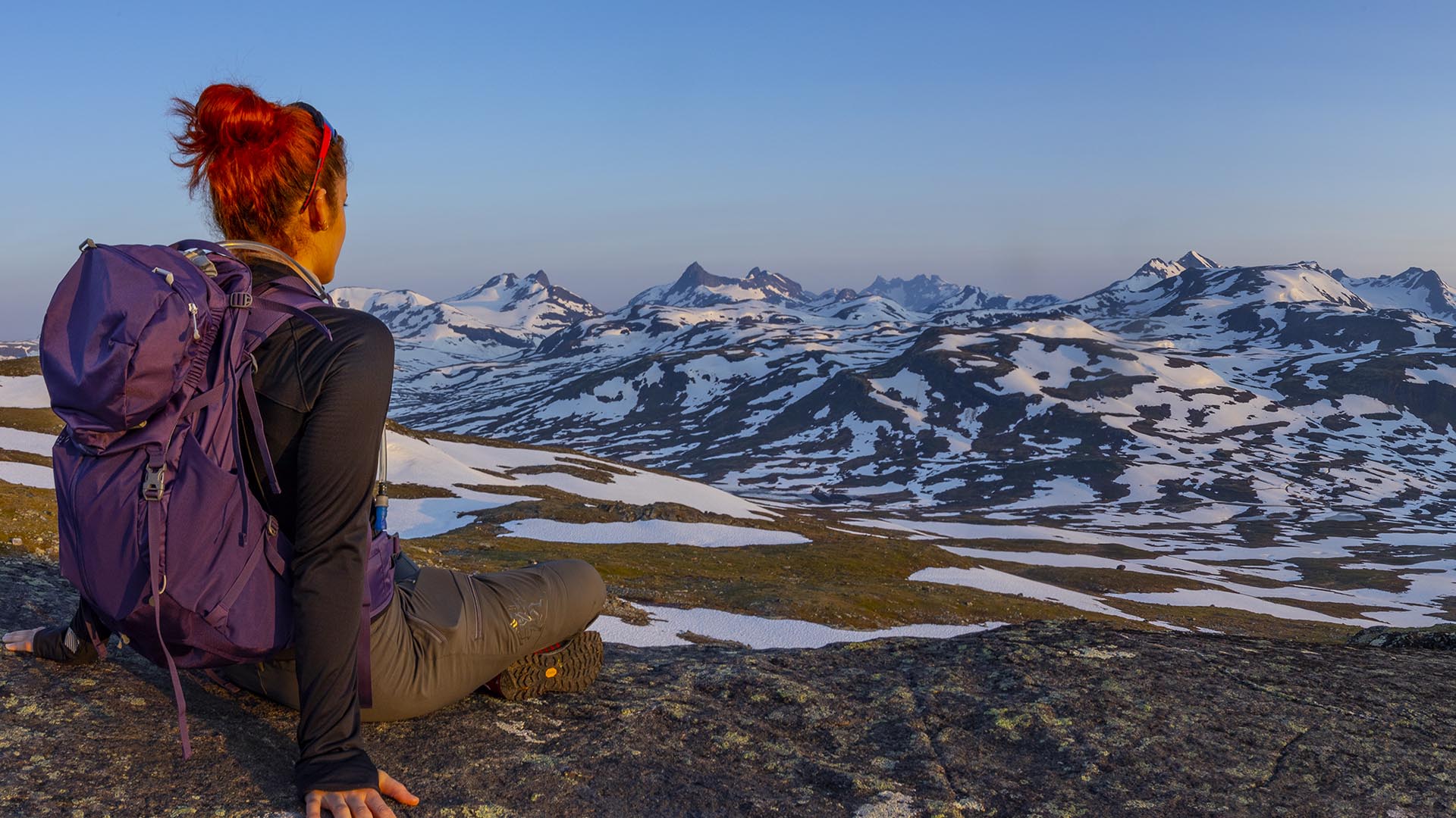 Women up close seen from behind while enjoying view towards snow patched mountains.